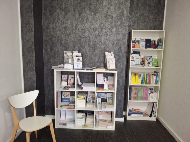Ein Stuhl und zwei weiße Regale mit Informationsmaterialien.